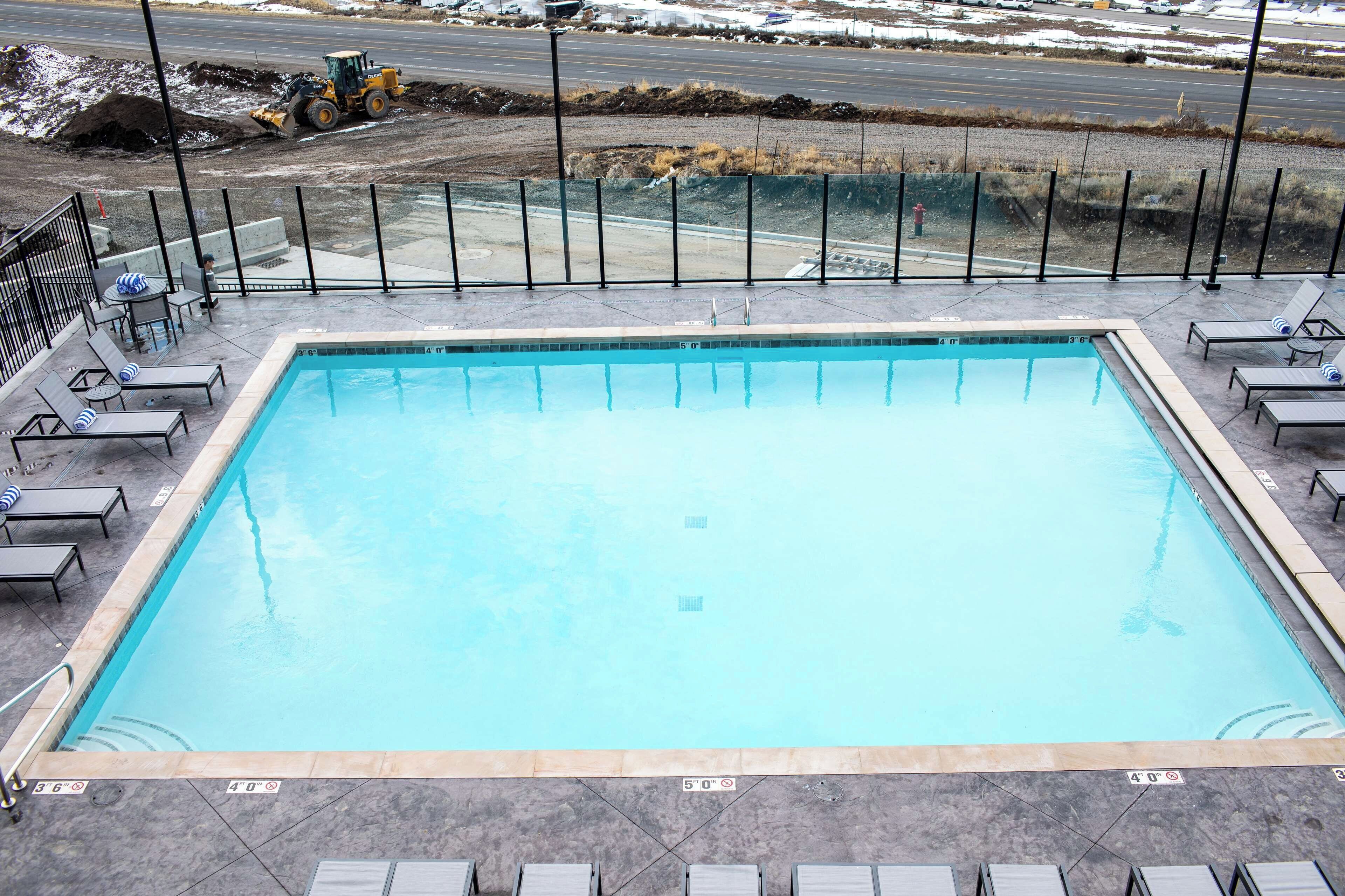 Una piscina rettangolare con acqua cristallina, circondata da sdraio e una recinzione di sicurezza.
