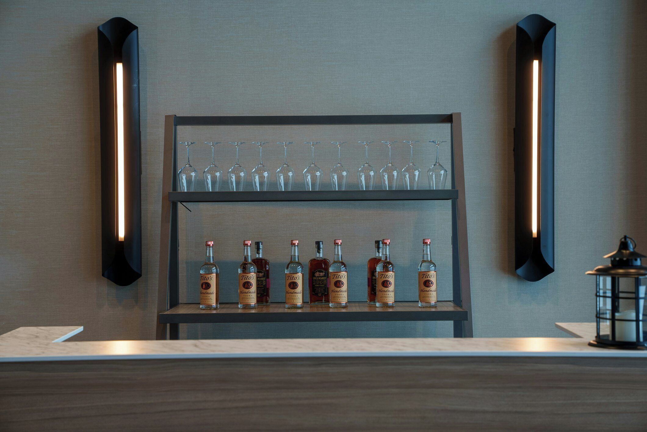 A bar area with a shelf holding glasses and bottles of Tito's Handmade Vodka.