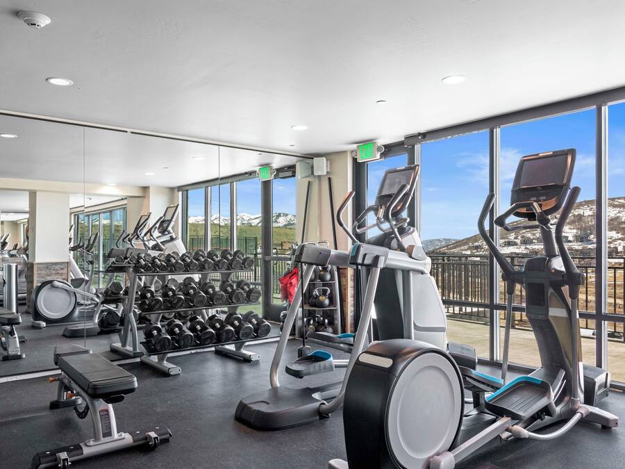 A gym with exercise equipment, a weight rack, and a view of a snowy landscape through large windows.