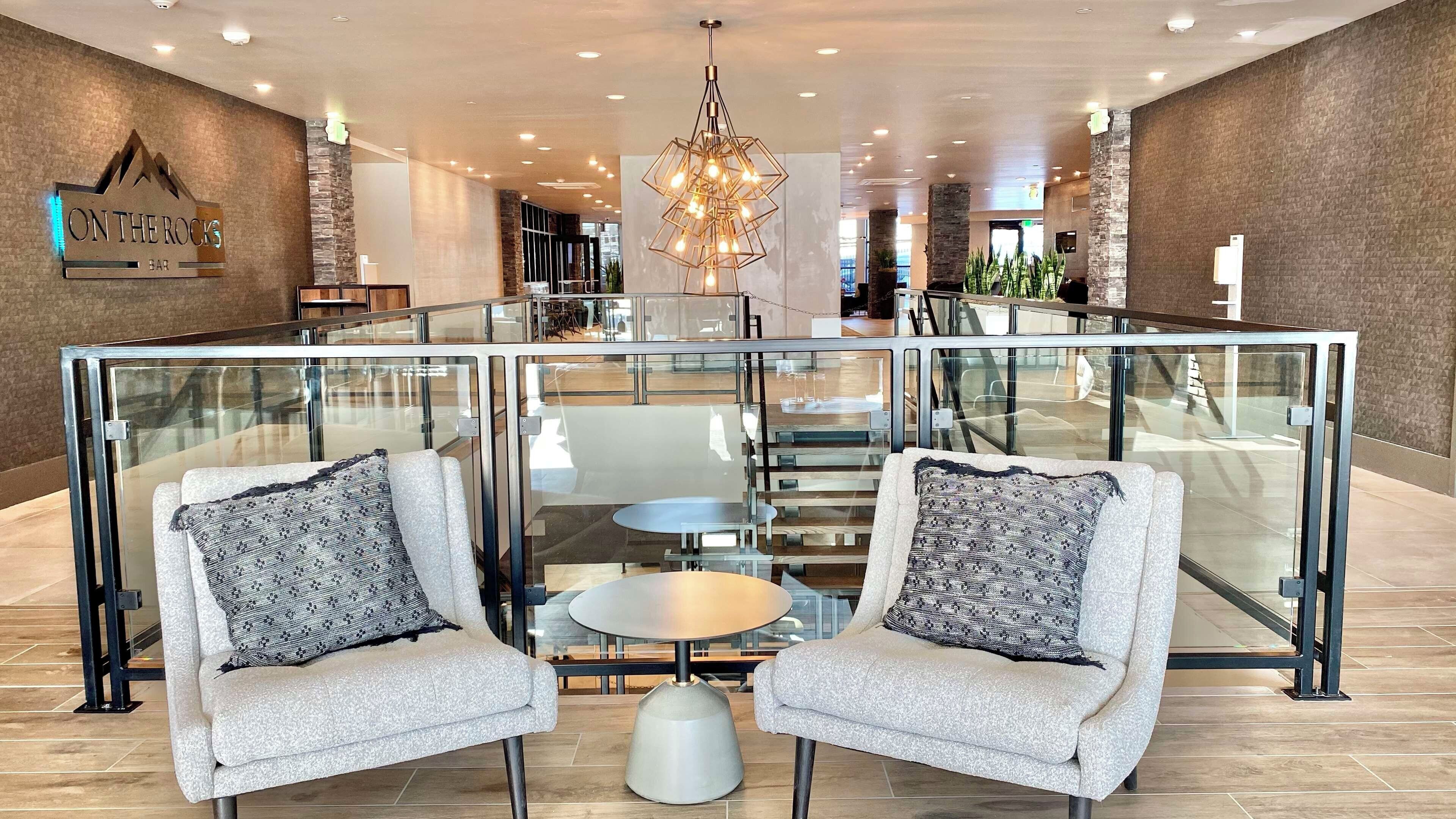 Un espacio lounge moderno con dos sillones, una partición de vidrio y una mesa central.