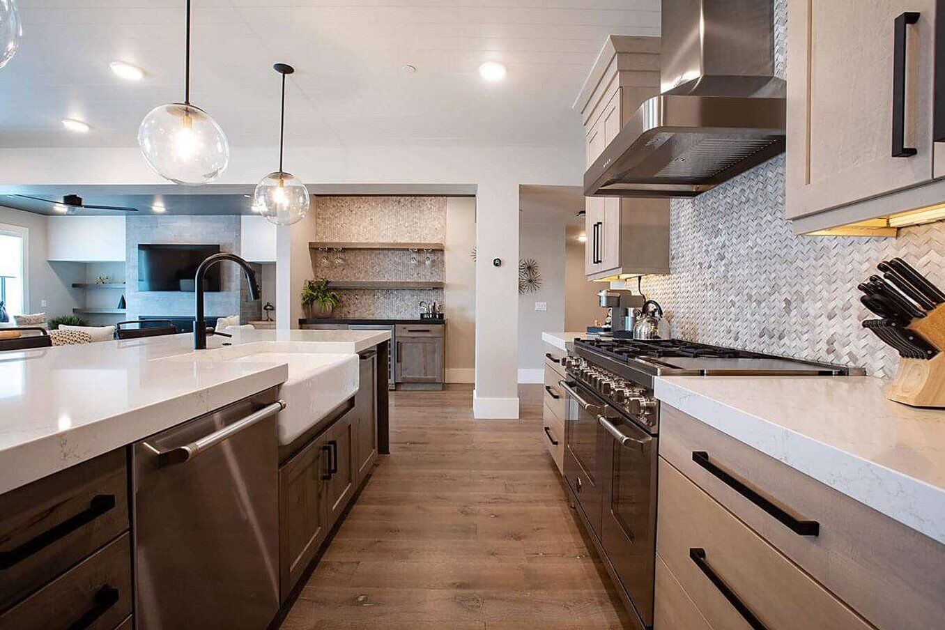 Une cuisine moderne dotée d’appareils électroménagers en acier inoxydable, d’un îlot central, de luminaires suspendus et d’un dosseret orné d’un motif en chevrons.