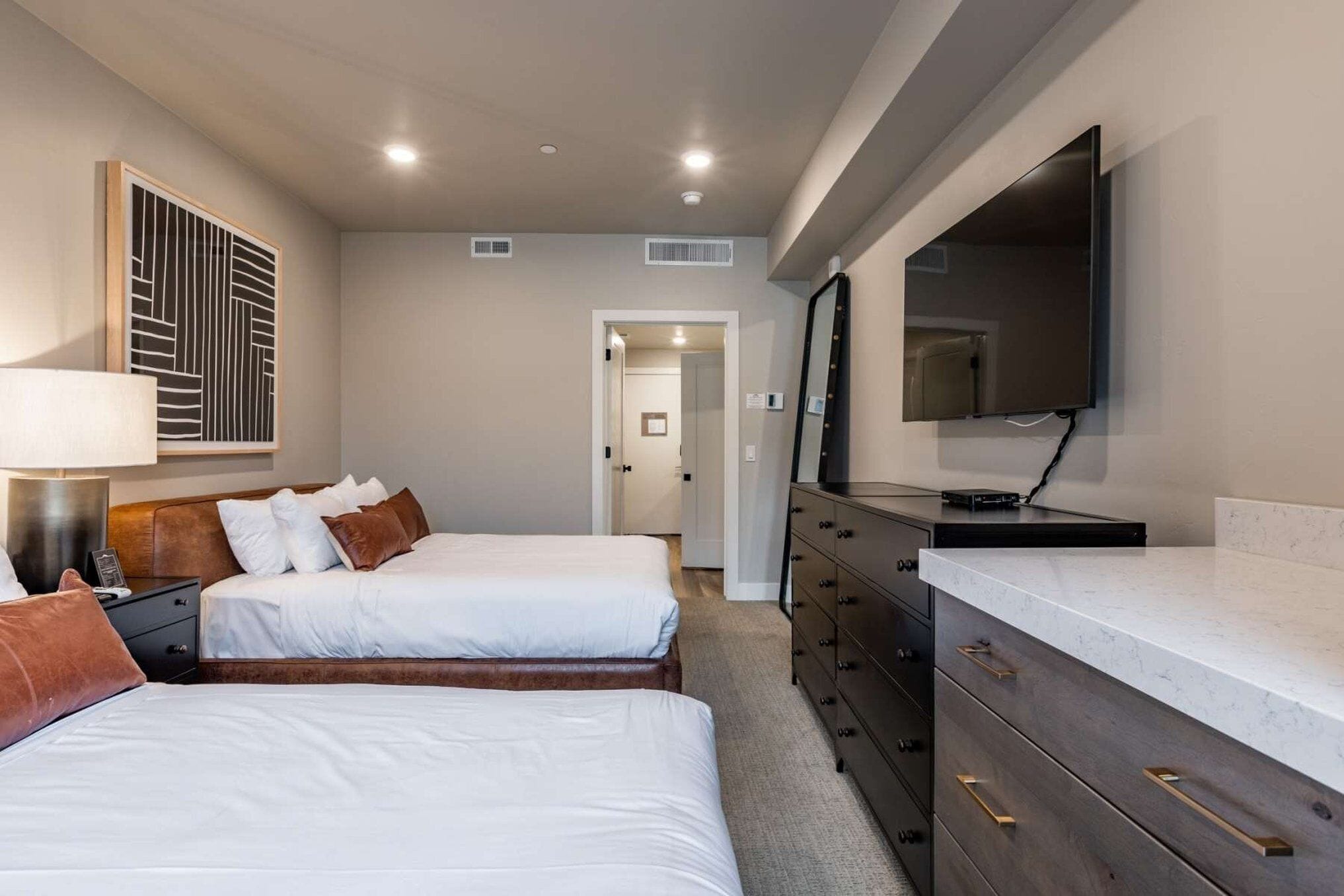 A hotel room with two beds, a dresser, a TV, and a mirror.