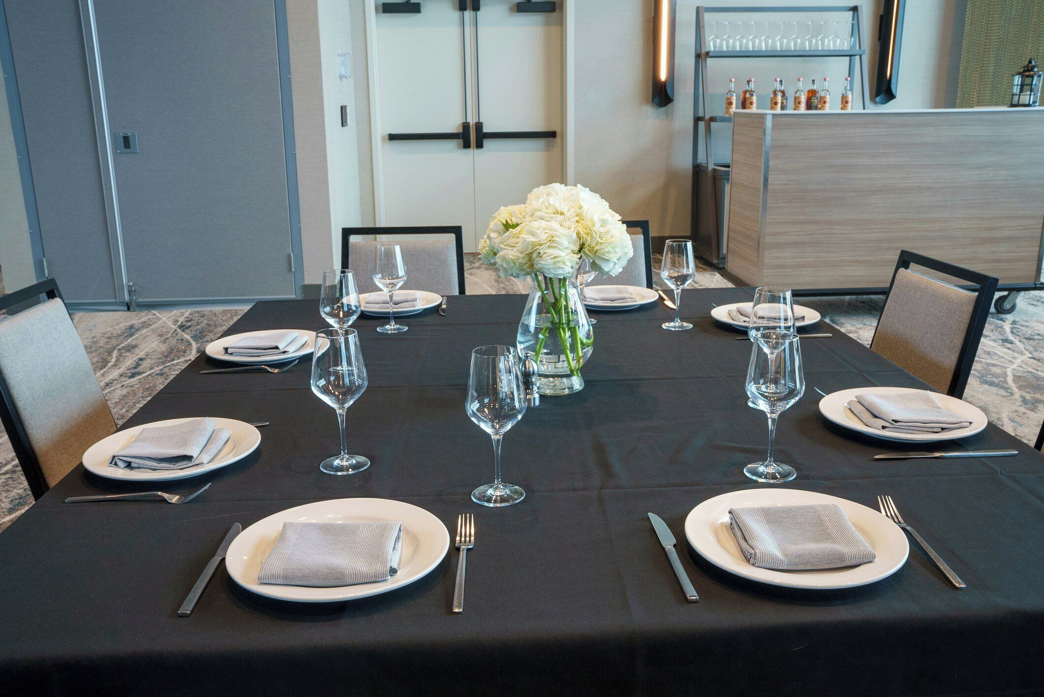 A dining table set with plates, cutlery, and wine glasses, with a vase of flowers in the center.
