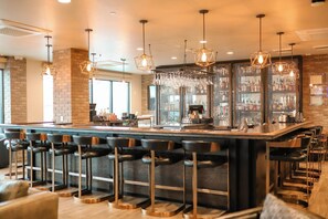 A modern bar area with a central island, multiple bar stools, pendant lighting, and a brick wall backdrop. - Black Rock Mountain Resort (Heber City)