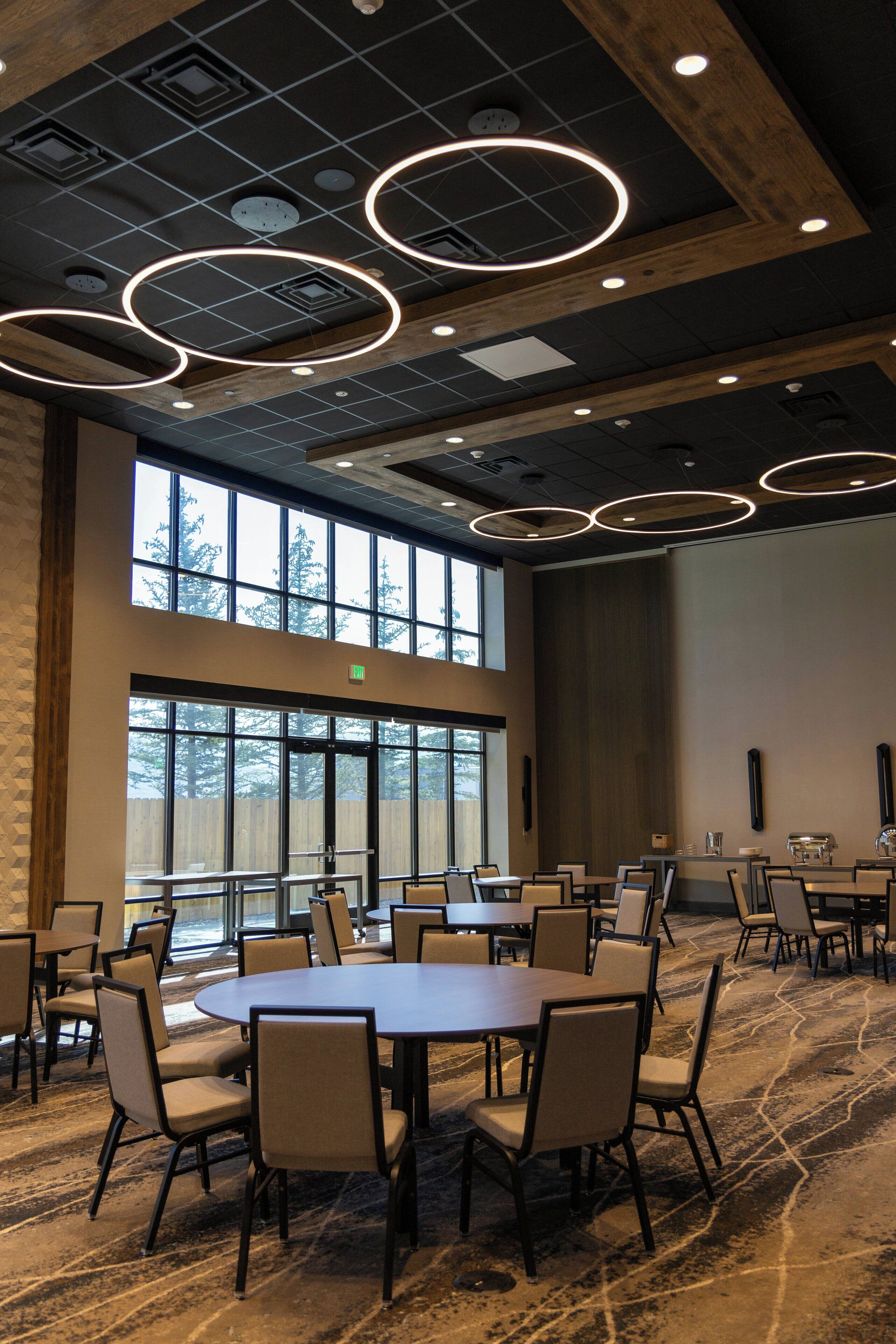 A conference room with round tables and chairs, large windows, and a modern ceiling design with circular light fixtures.