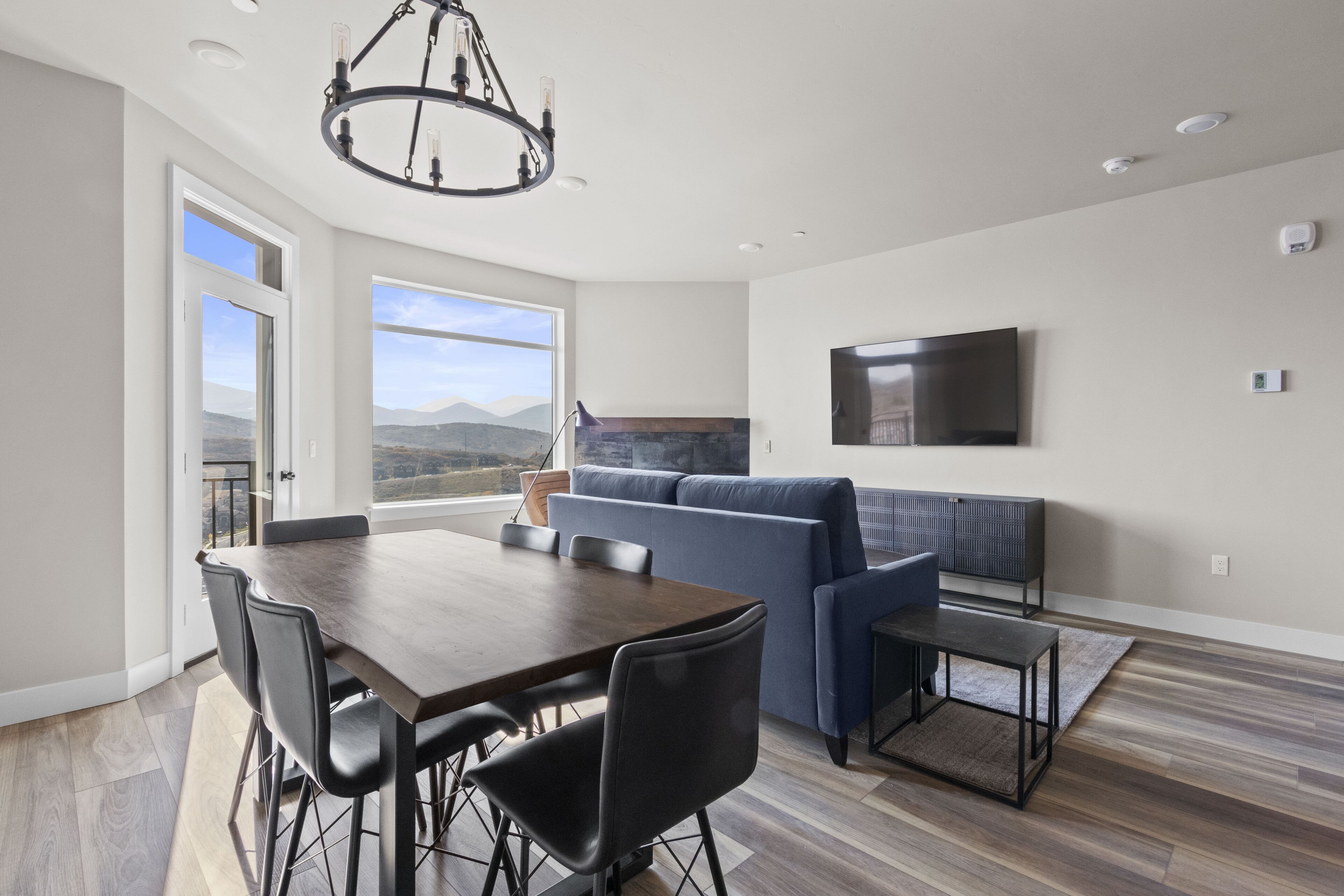 Una sala de estar moderna con una mesa de comedor, sillas, un sofá y un televisor montado en la pared.