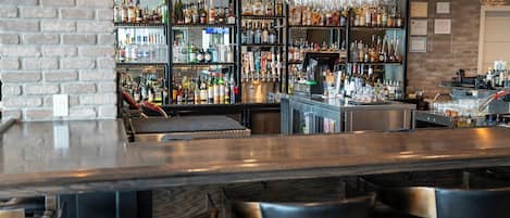 Eine Bar mit Ziegelwand, Regalen voller Spirituosenflaschen und einer Theke mit Hockstühlen.