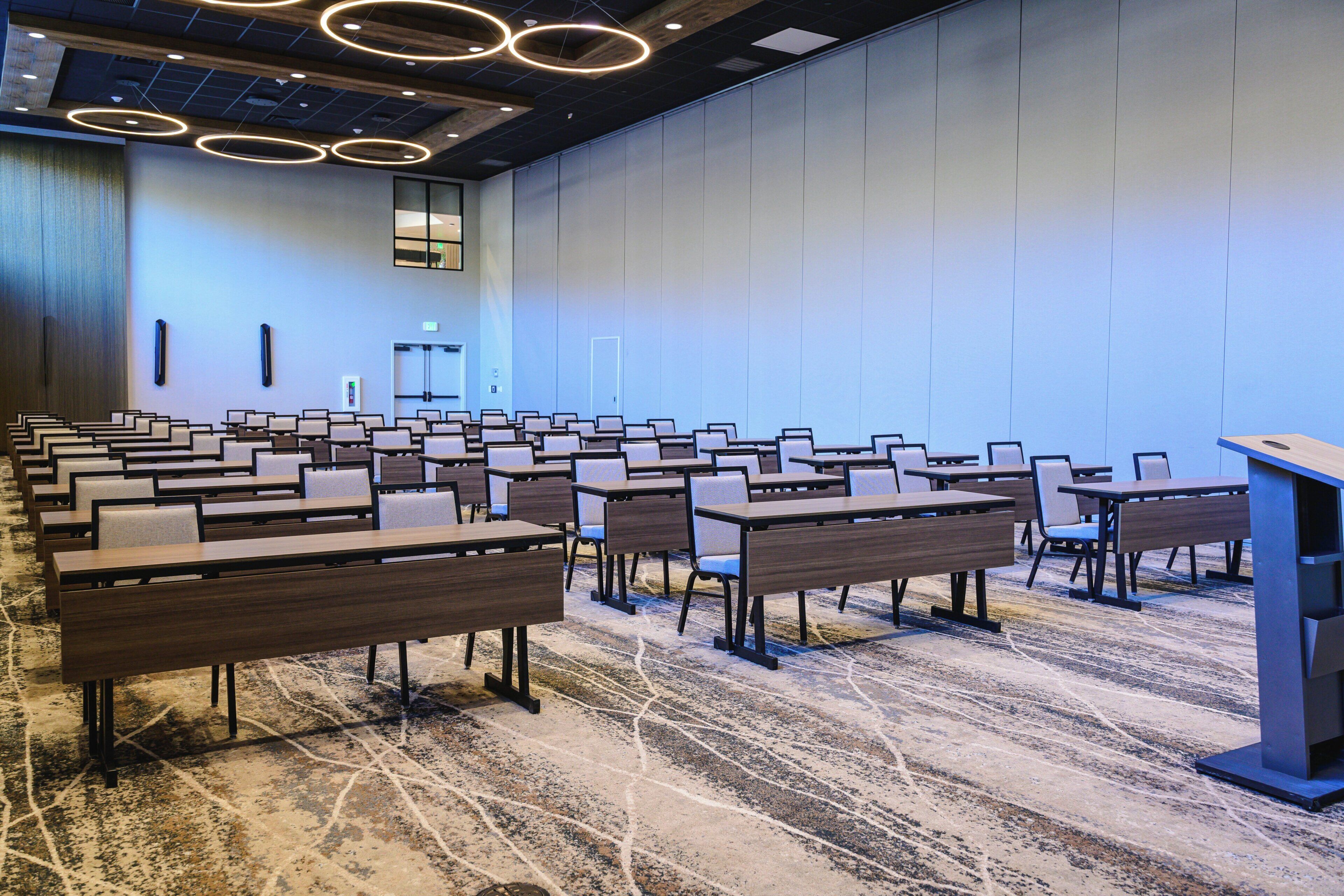 A conference room with rows of tables and chairs, a podium, and a carpeted floor.