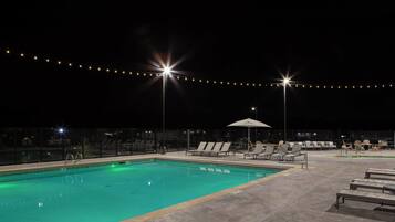 A swimming pool with lounge chairs and umbrellas, surrounded by a fence and string lights.