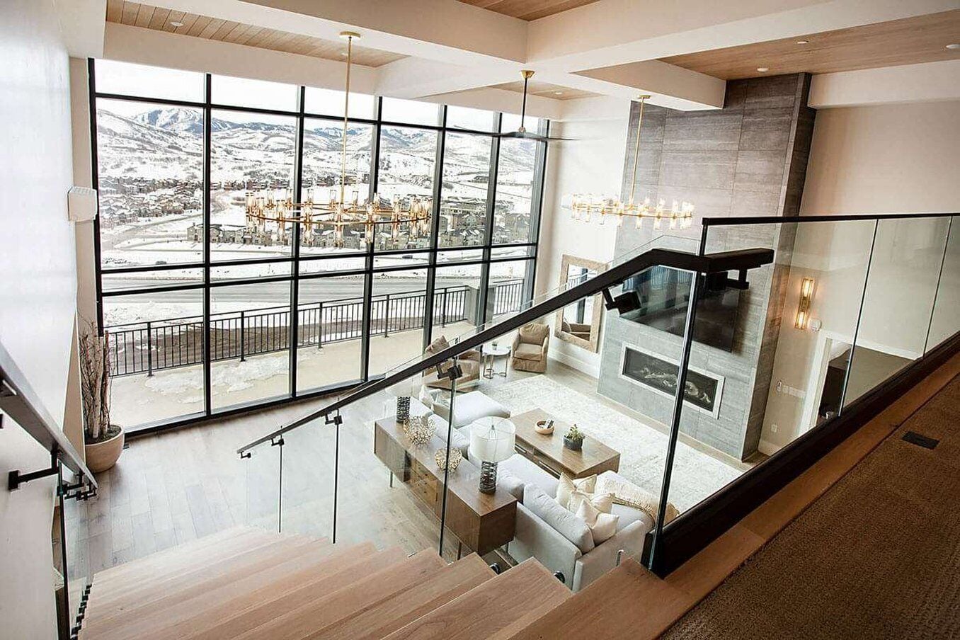 Ein modernes Interieur mit einer Treppe, die in einen Wohnbereich mit Kamin führt, große Fenster bieten Blick auf eine verschneite Landschaft.