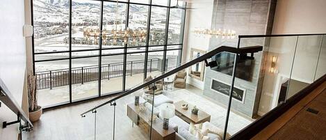 A modern interior with a staircase leading to a living area with a fireplace, large windows offering a view of a snowy landscape.