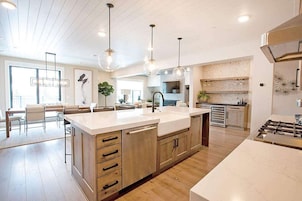 A modern kitchen with a large island, wooden cabinets, and pendant lighting.