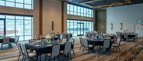 A conference room with multiple tables set for dining, large windows, and a modern ceiling design.