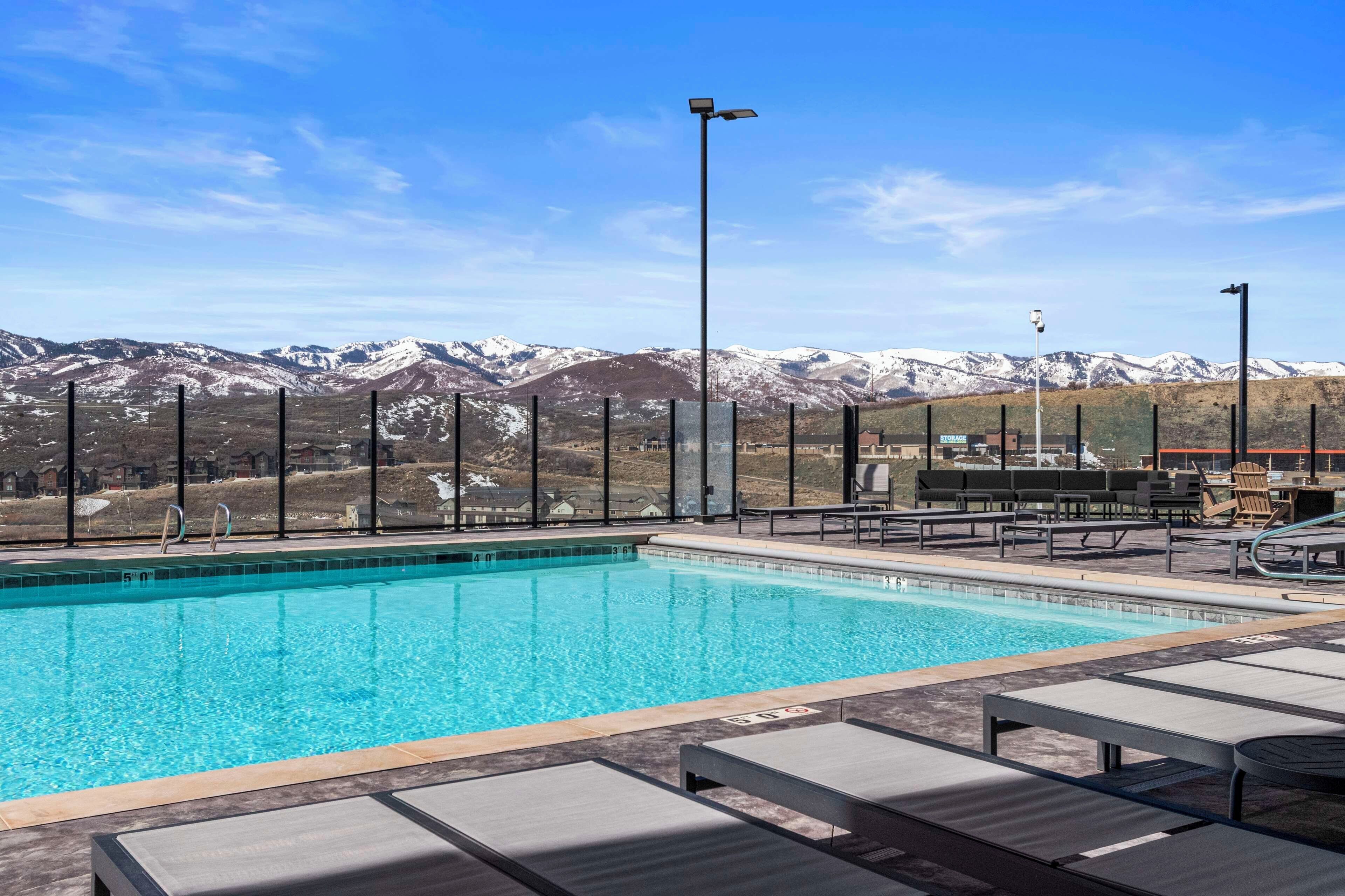 Piscina cristallina blu con sedie a sdraio e vista sulle montagne innevate.