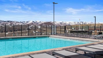 Piscina cristallina blu con sedie a sdraio e vista sulle montagne innevate.