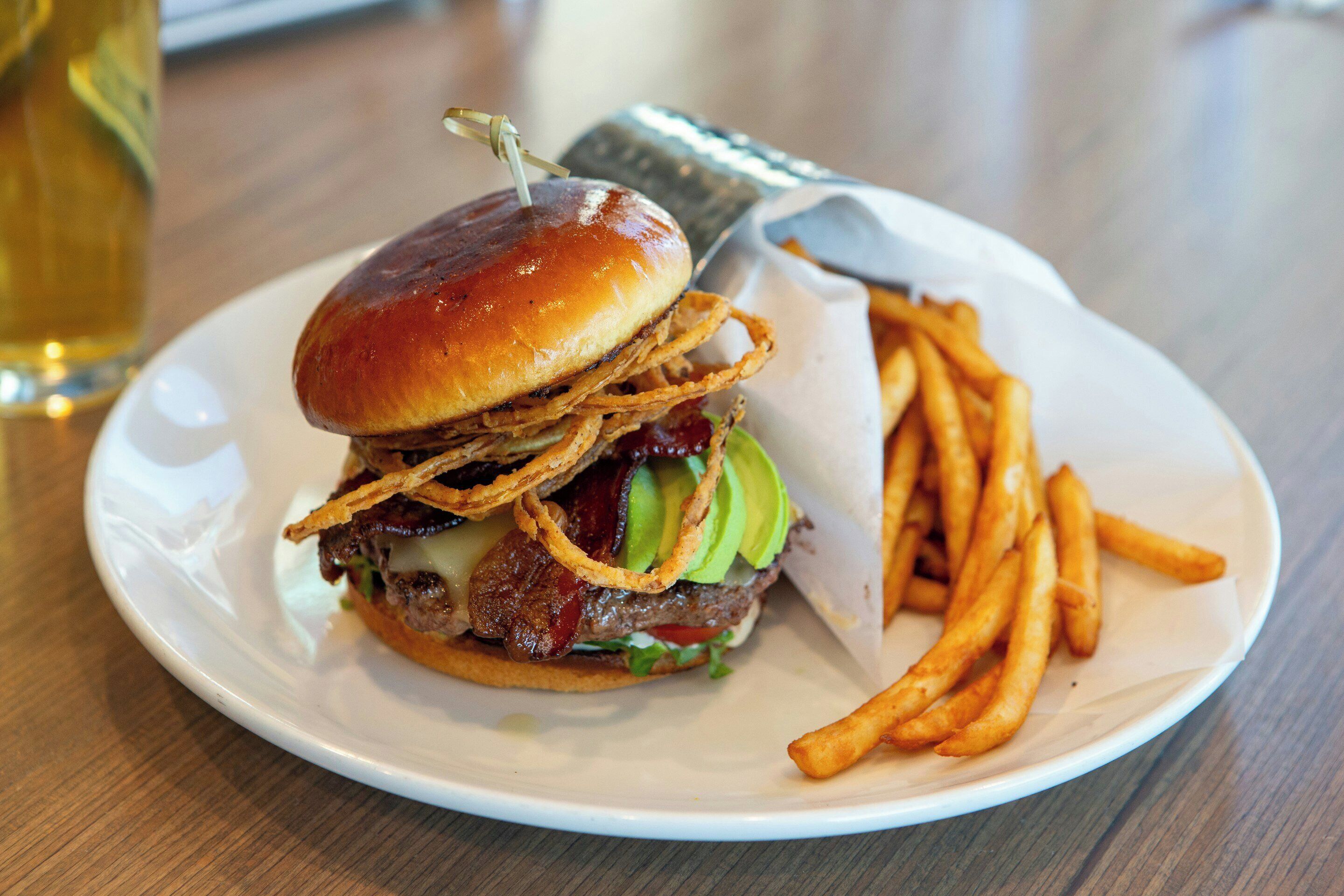 Een bord met een hamburger, friet en een drankje.