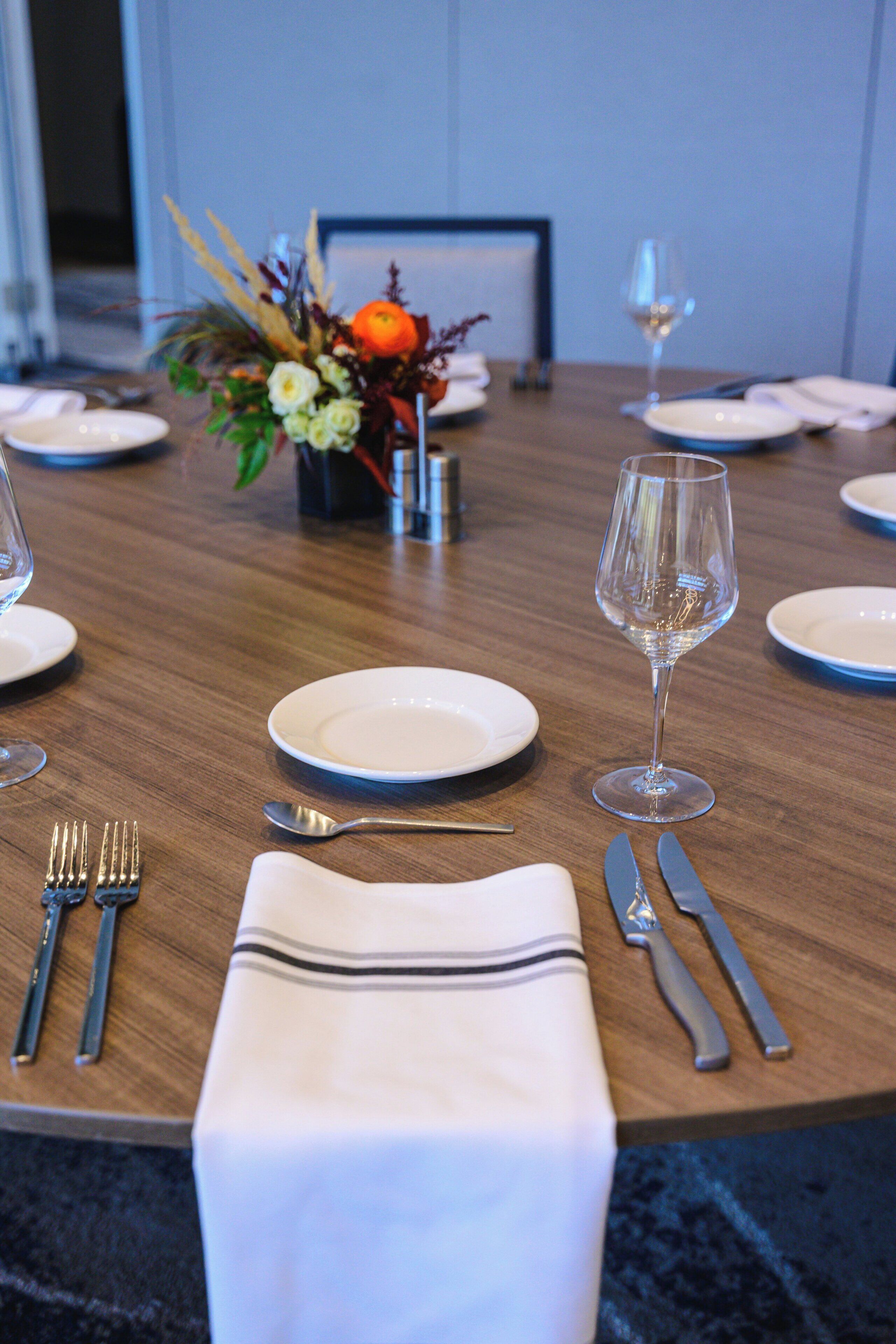 A dining table set with plates, cutlery, a glass, and a folded napkin.