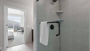 A modern bathroom with a glass shower enclosure, a towel rack, and a view of a balcony with a bed and a chair.