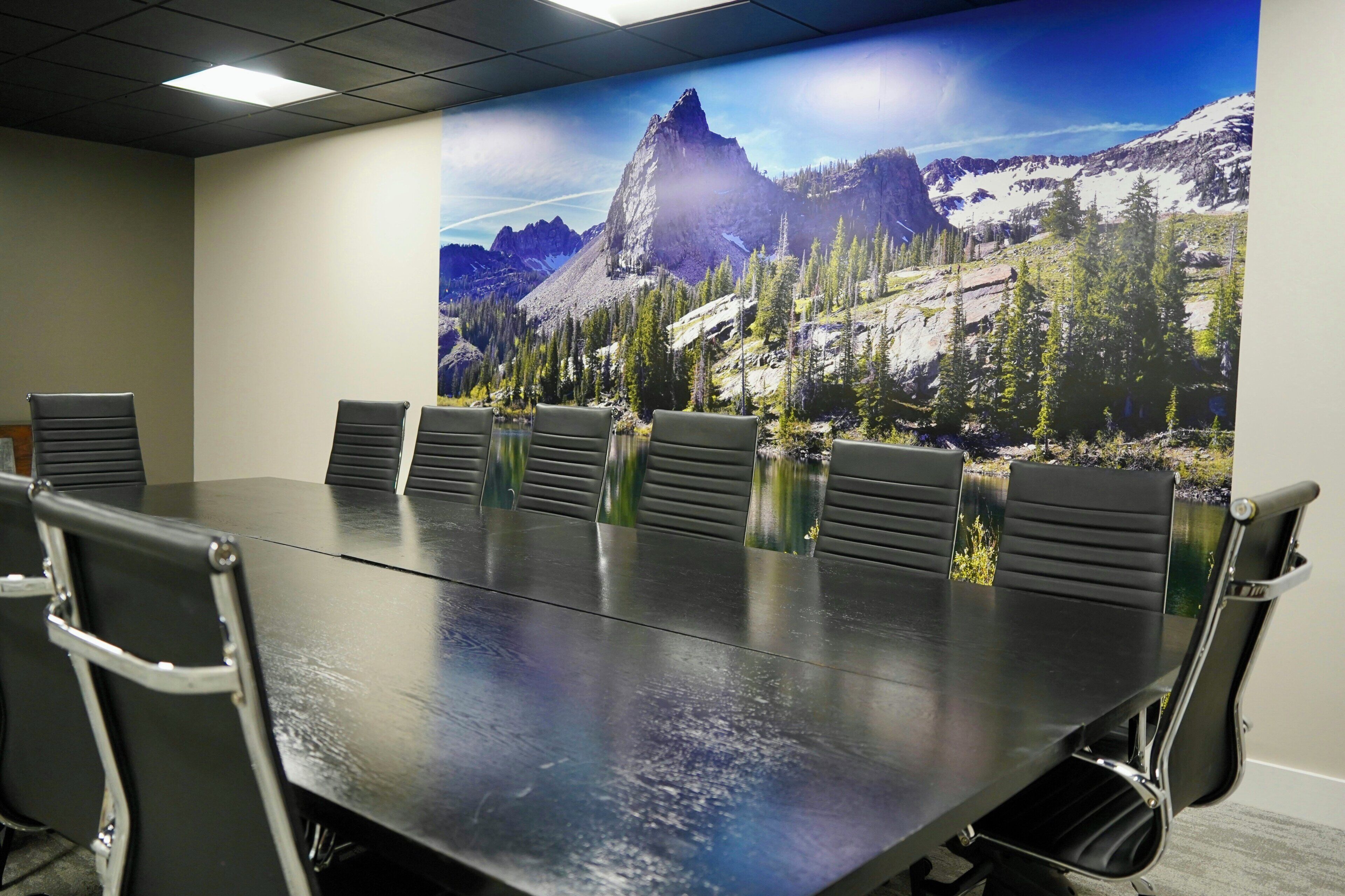A conference room with a long table and six chairs, a large window with a mountain view, and a ceiling with recessed lighting.