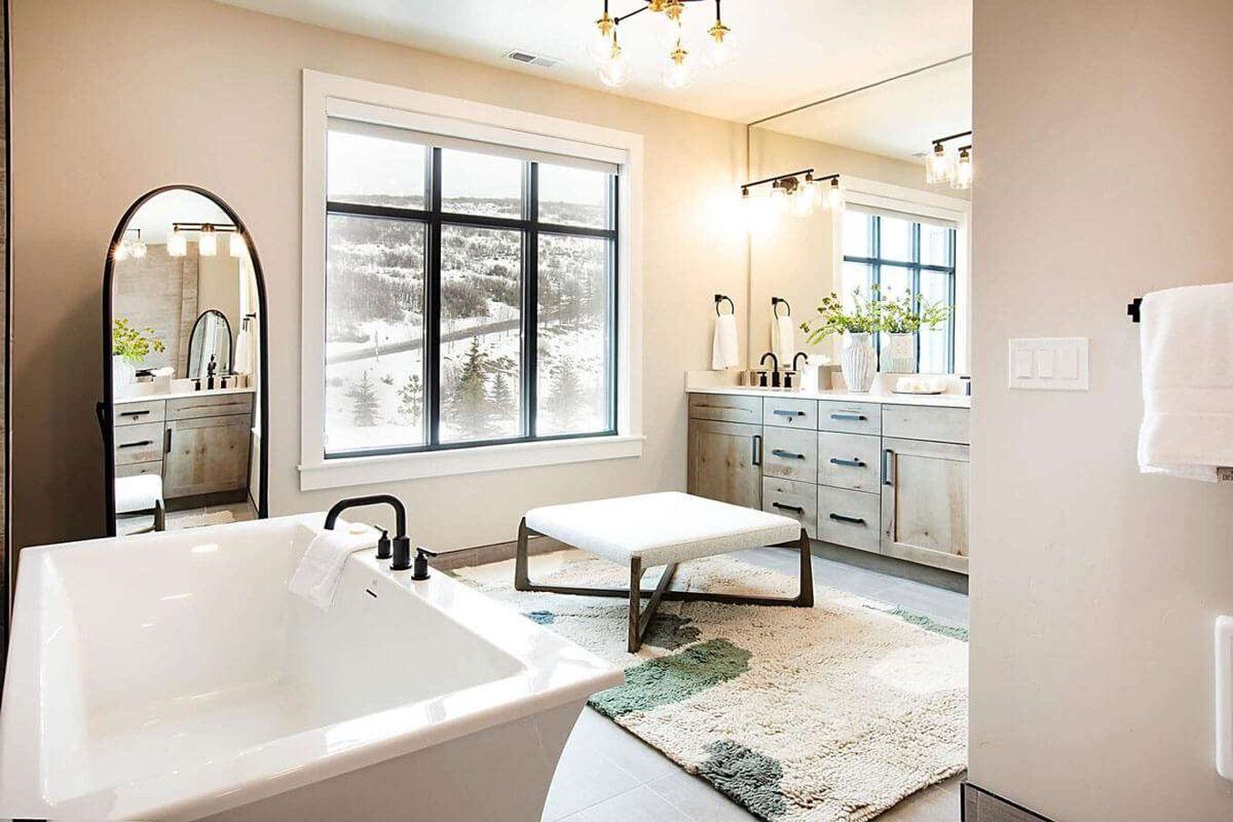 A modern bathroom with a large bathtub, a window with a view of a snowy landscape, a mirror, and a sink with a towel rack.