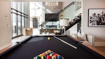Uma sala de estar moderna com mesa de bilhar, escada e uma grande janela.