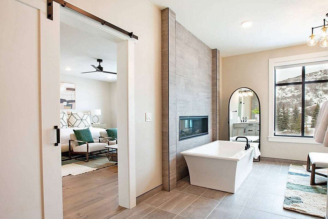 A modern bathroom with a freestanding bathtub, a large mirror, and a window providing a view of the outdoors.