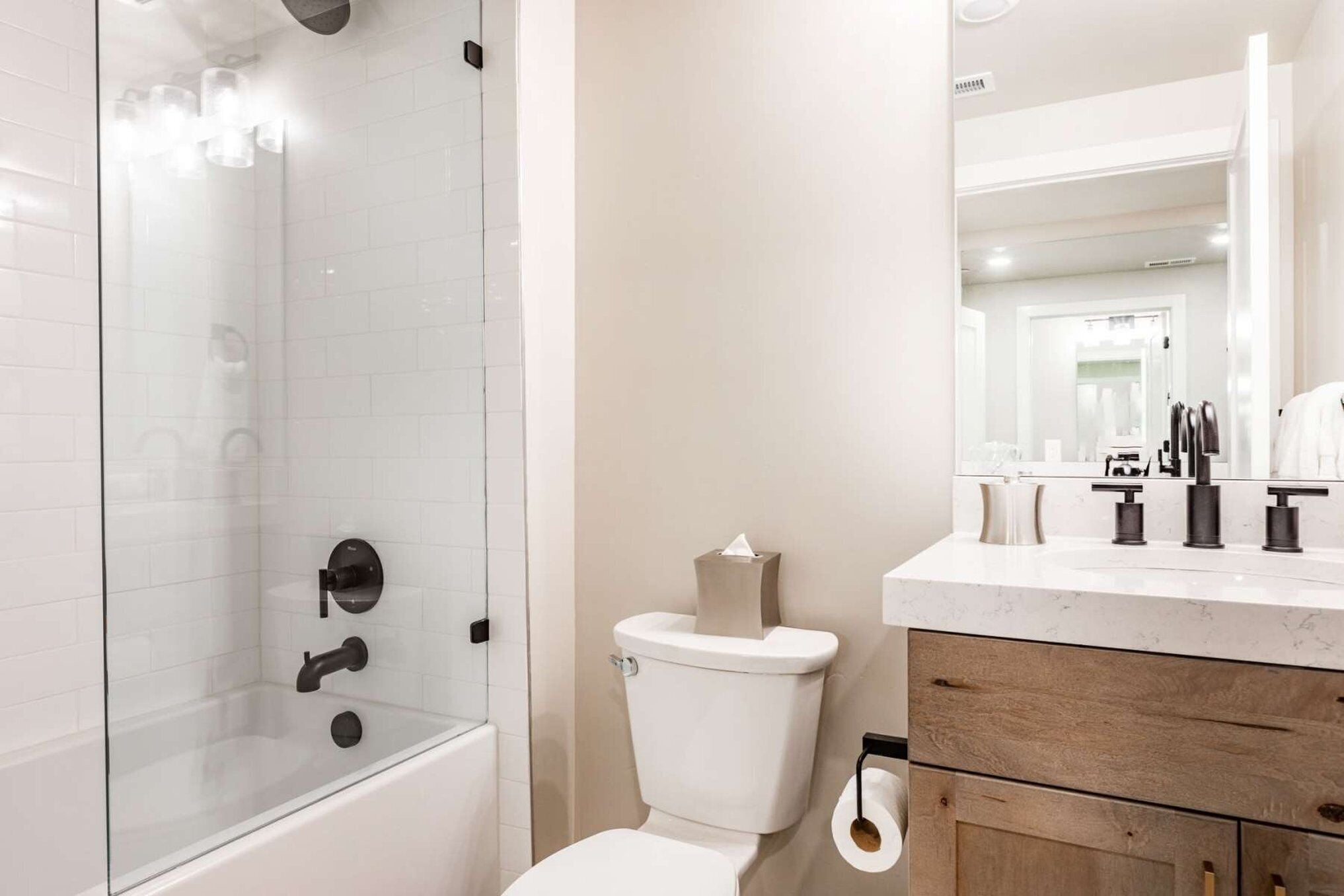 Un baño moderno con ducha de mampara de vidrio, inodoro y tocador con espejo.