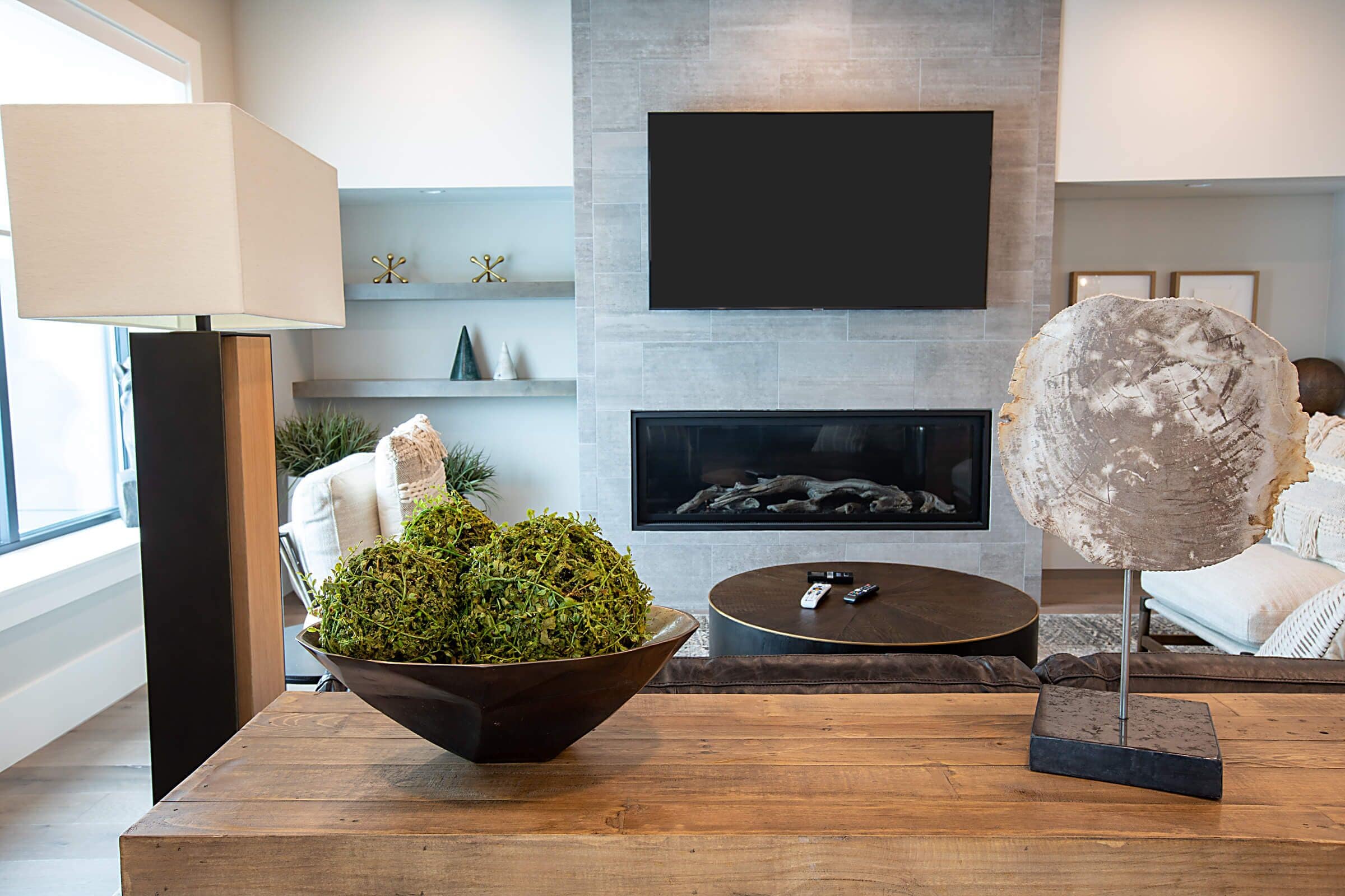 Una sala de estar moderna con chimenea, un televisor de pantalla plana montado encima, una mesa de centro de madera y una escultura decorativa de piedra.