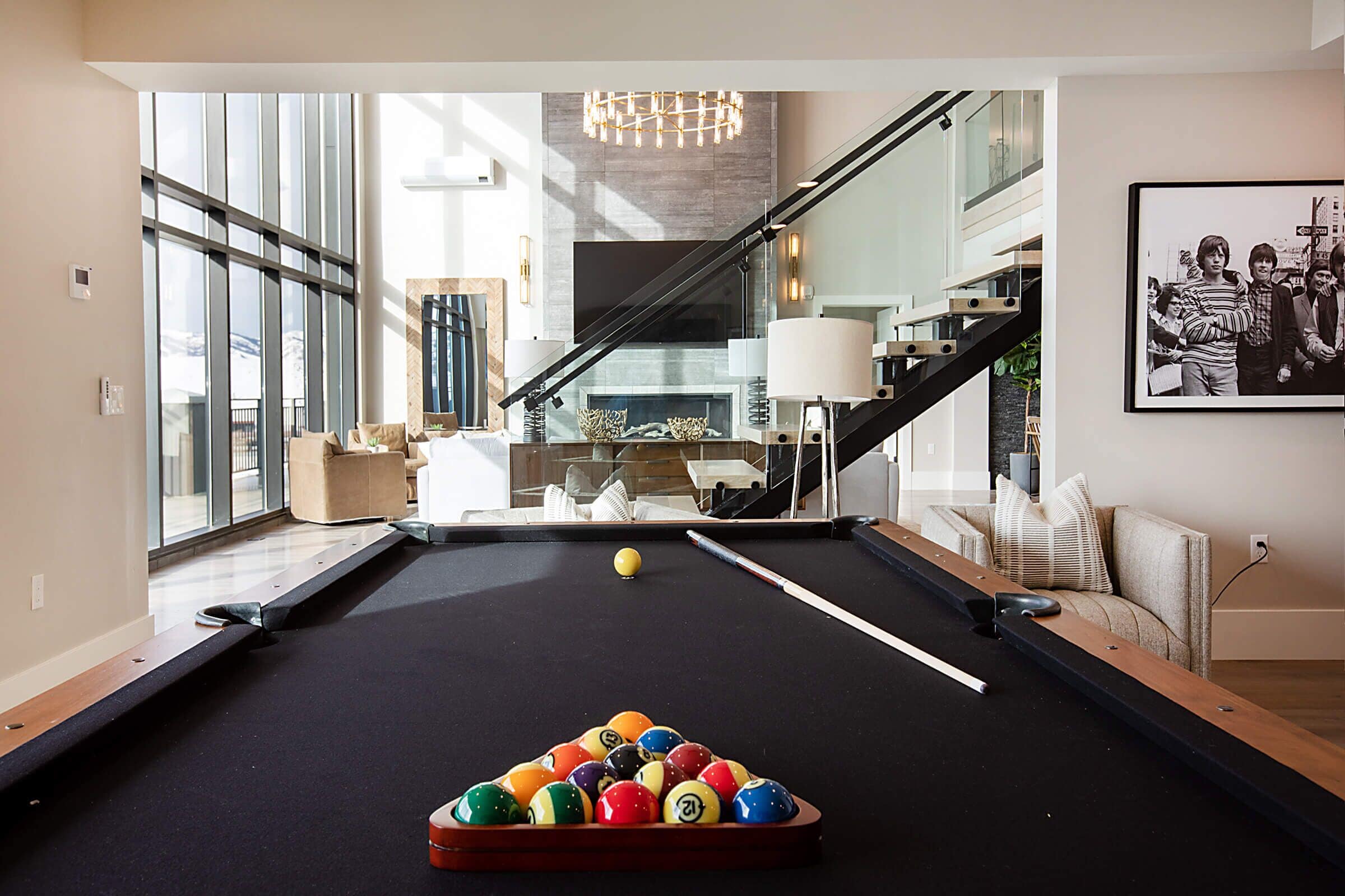 A modern living room with a pool table, a staircase, and a large window.