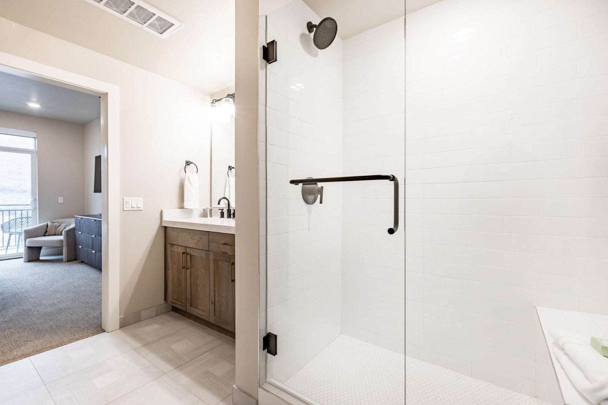 A modern bathroom with a glass shower enclosure, a white sink, and a towel rack.