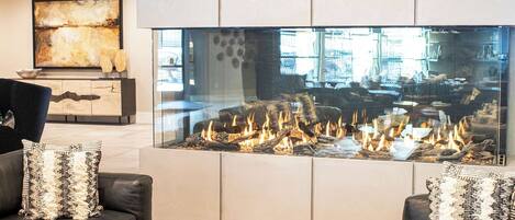 Una sala de estar moderna con chimenea de vidrio, sofás de cuero y una lámpara araña contemporánea.