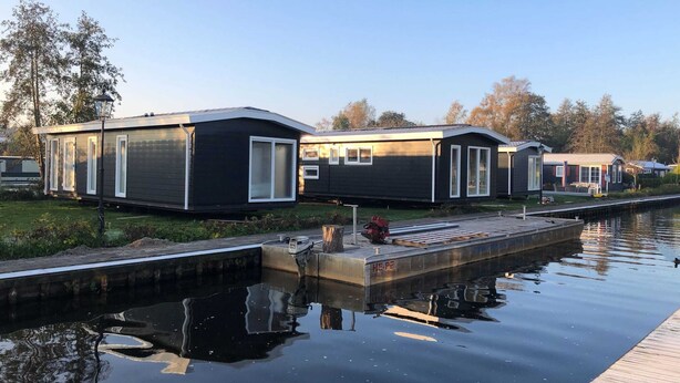 Een rij moderne, donkergekleurde stacaravans met witte accenten, gelegen naast een rustige gracht.