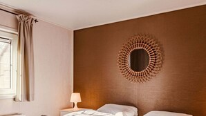Een hotelkamer met twee bedden, een spiegel aan de muur, een bedlampje en een raam met gordijnen.