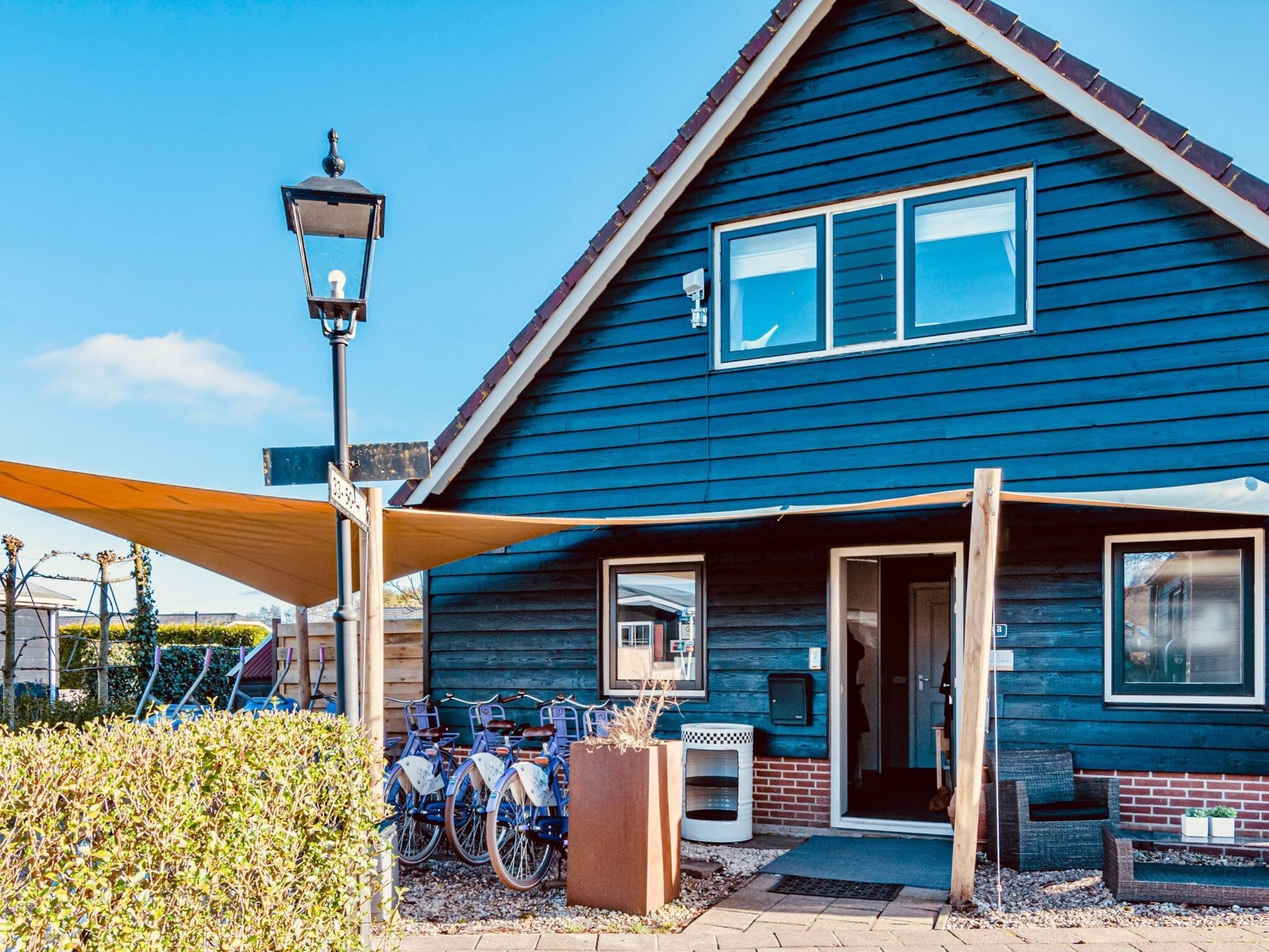 En blå träbyggnad med ett sluttande tak, en veranda med en bänk och ett cykelställ utanför.