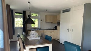 A modern kitchen with a dining area, featuring a wooden table, blue chairs, and a hanging light fixture.