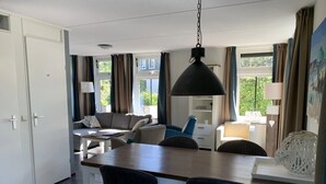 A modern living room with a dining area, featuring a sofa, chairs, a table, and a hanging pendant light.