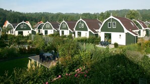 A row of green and white cottages with a garden area in the foreground.