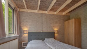 Une chambre avec un lit, une armoire, une fenêtre avec des rideaux et un mur en briques.