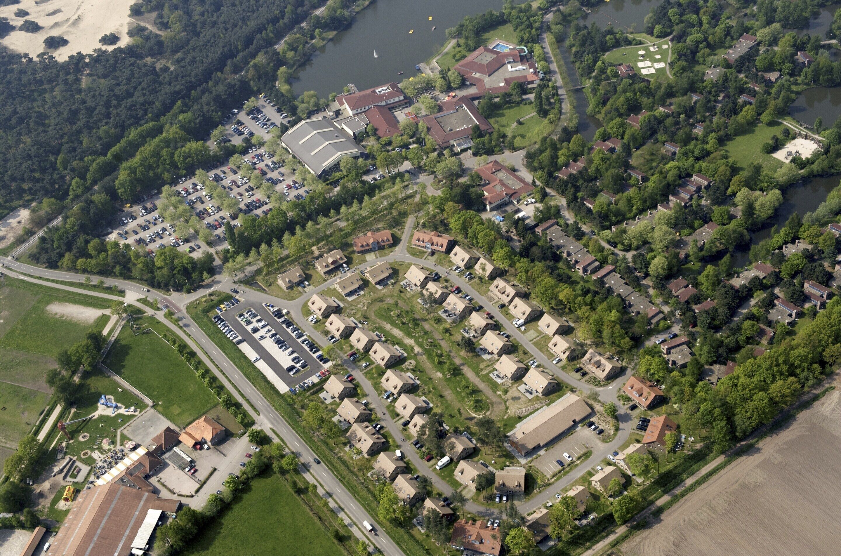 An aerial view of a residential area with houses, a parking lot, and a river.