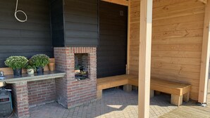 Un espace barbecue extérieur en briques, agrémenté d’un banc en bois et de plantes en pot.