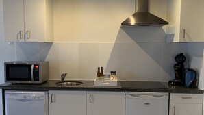 Une cuisine moderne avec des meubles blancs, un four à micro-ondes en acier inoxydable, une machine à café et un lave-vaisselle.