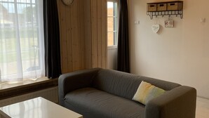 Une pièce avec un canapé gris, une table blanche, une horloge murale et une fenêtre avec des rideaux.