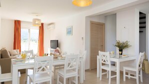 A dining area with a glass table, white chairs, a television, and a view of the outdoors. - Apartment in the Hilly Landscape of Oletta (Oletta)