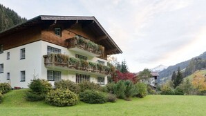 A two-story chalet with wooden balconies, surrounded by lush greenery and mountains in the background. - Apartment in Grossarl Near Ski Slopes (Grossarl)