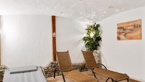 A room with a massage table, two wicker chairs, a potted plant, and a painting on the wall. - Apartment in Grossarl Near Ski Slopes (Grossarl)