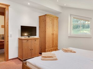 A bedroom with a bed, a wooden wardrobe, a television on a stand, and a window with a view of greenery. - Apartment in Grossarl Near Ski Slopes (Grossarl)