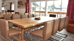 A dining area with a wooden table and leather chairs, large windows with a view of a snowy landscape, and a painting on the wall. - Luxury Chalet in Saalbach-Hinterglemm near Ski Area (Saalbach-Hinterglemm)