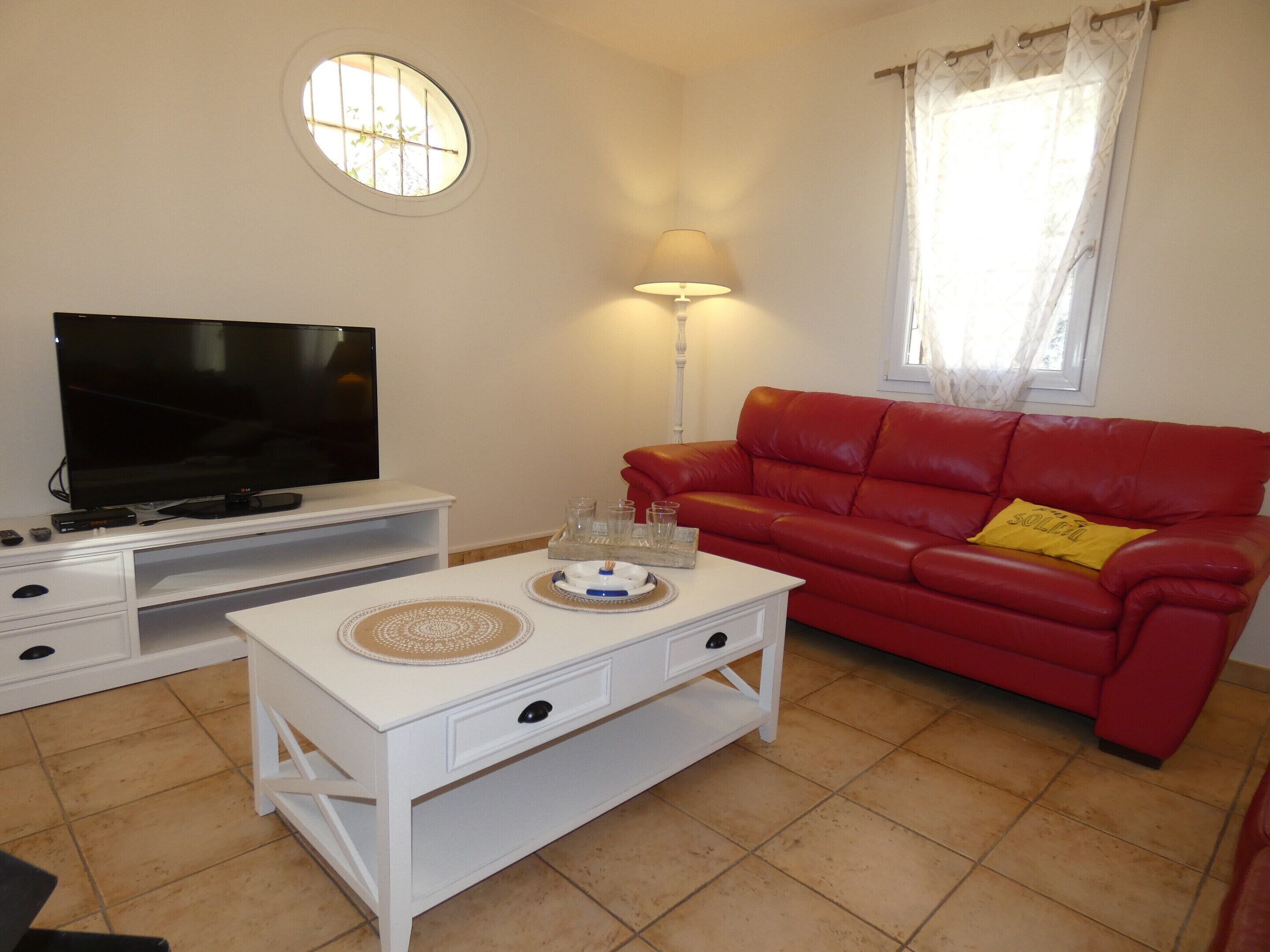 A living room with a television on a stand, a red sofa, a white coffee table, and a lamp.
