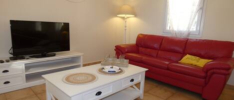 A living room with a television on a stand, a red sofa, a white coffee table, and a lamp.
