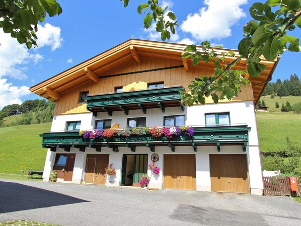 A two-story chalet with a wooden facade, green balconies, and flower boxes.